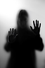 Mysterious figure standing behind a foggy glass in a dimly lit space during late evening hours