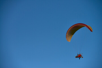Caucasian young adult man piloting powered paraglider against clear blue sky, holding controls while flying solo, engaging in adventure sport, copy space on left side