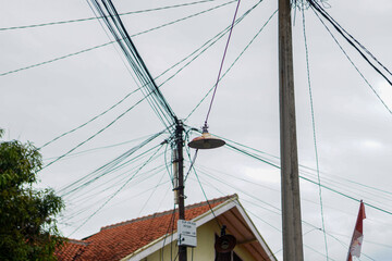 Captured from a low angle, a network of chaotic cables and utility poles against a backdrop of a cloudy sky, features overhead power lines weaving haphazardly, isolated in white background.