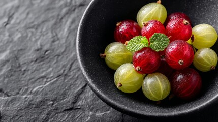 Fresh red and green gooseberries in black bowl on slate surface