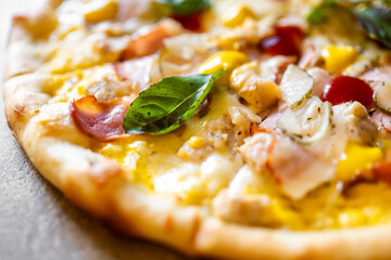 Close-up of freshly baked pizza with melted cheese, ham, cherry tomatoes, bell peppers, mushrooms, and basil on golden crust. Vibrant colors, appetizing food presentation