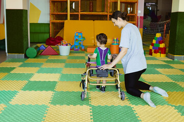 Professional physical therapist assists young boy patient as he uses a walker in a bright and supportive therapy environment