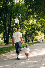 Rear view, from the back. Father that is amputee with prosthesis is with his little son in the park