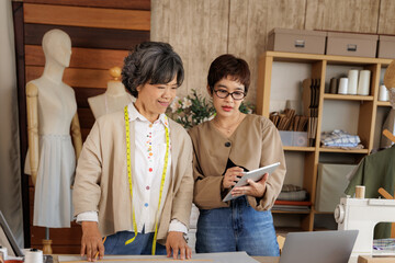 two Asian women working together in a clothing design studio.