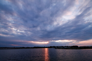 Dramatic Cloudy Sunset Over a Serene Coastal Harbor with Sailboats Moored and Reflective Water