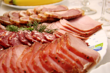 An appetizing arrangement of diverse sliced cold meats, such as ham, salami, and various cured selections, elegantly garnished with fresh dill on a serving platter, perfect for a festive occasion.
