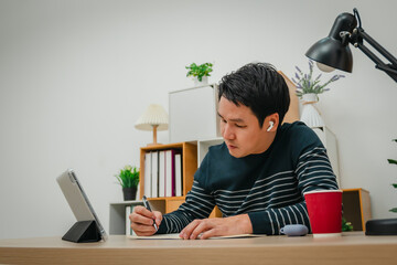 man learning online with tablet and wireless earbuds at home office