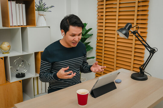 stressed man using digital tablet and wireless earbuds making video call in home office