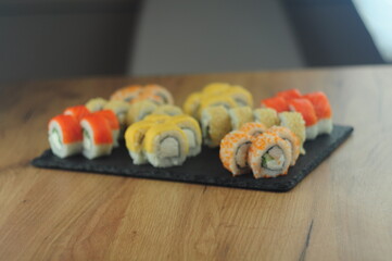 Sushi set on black stone plate, assorted Japanese rolls with salmon, tobiko, cream cheese, cucumber, sesame and sauce, traditional Asian cuisine