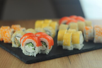 Sushi set on black stone plate, assorted Japanese rolls with salmon, tobiko, cream cheese, cucumber, sesame and sauce, traditional Asian cuisine