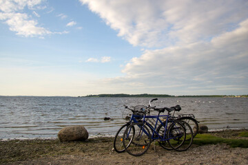 Fototapeta premium Two blue bicycles parked on a tranquil lakeside shore under a partly cloudy sky