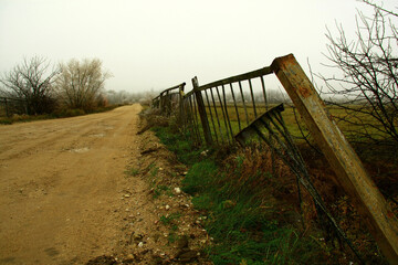 A winding dirt path alongside an old weathered fence on a foggy morning