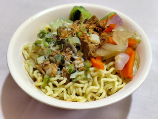 A bowl of delicious chicken noodles, complete with claws, dumplings, chicken pieces on top, traditional Indonesian food.