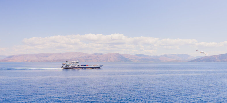 passenger ferry crossing calm blue sea with seagull and mountainous horizon under partly cloudy sky. - Powered by Adobe