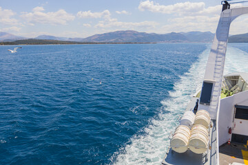 Ferry wake trails across deep blue sea toward coastal mountains and sky