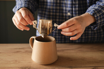 Woman hand holding cup with black coffee and drip filter on kitchen table.