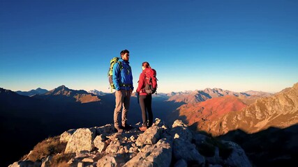 Experienced mountain hikers reaching alpine summit during golden sunset, sharing breathtaking landscape moment with panoramic wilderness view and sense of achievement