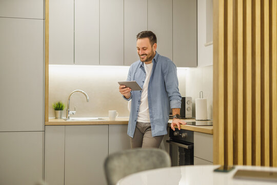Man enjoys using a tablet while relaxing in a modern kitchen during daytime