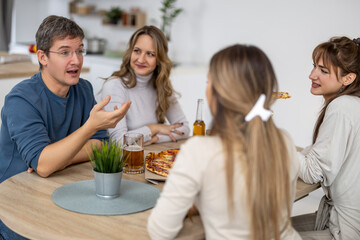 Friends enjoy pizza and drinks while having a lively conversation at a modern kitchen table during a cozy gathering