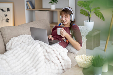 Woman relaxing on couch with laptop, coffee, and headphones in serene home setting