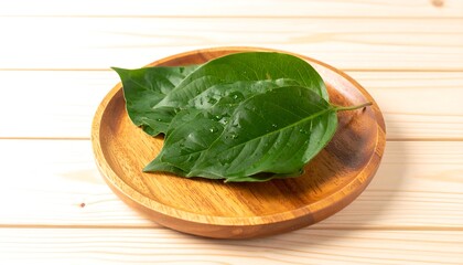 Fresh, vibrant green leaves rest on a light brown wooden plate, showcasing a natural and healthy aesthetic.