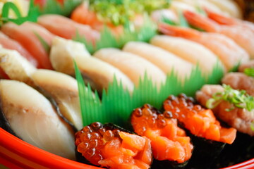 A beautifully arranged assortment of traditional Japanese sushi with fresh seafood including shrimp, salmon, tuna, and ikura, served in a festive round tray