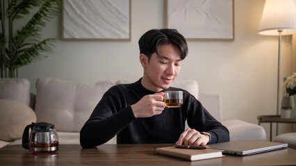Young man sipping tea during a relaxing break in his home office setup.