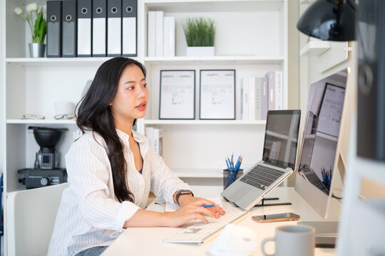Thoughtful female developer working at a desk with two monitors and a laptop.