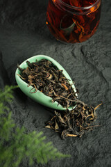 Organic loose leaf tea in ceramic spoon with brewed tea glass on dark slate background