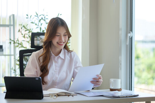 Cheerful young businesswoman reading documents while working in a bright home office.