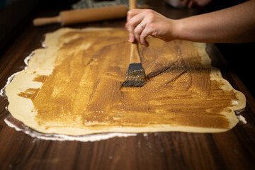 Hand applying cream on raw dough. Step in preparing sweet homemade pastries.
