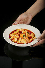 Fresh Handmade Pasta in Tomato Broth Bowl Held by Hands on Dark Background