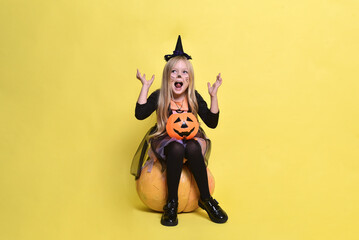 Cute little girl in a witch costume is sitting on a big pumpkin for Halloween.