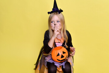 Cute little girl in a witch costume is sitting on a big pumpkin for Halloween.