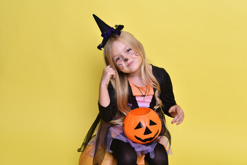 Cute little girl in a witch costume is sitting on a big pumpkin for Halloween.