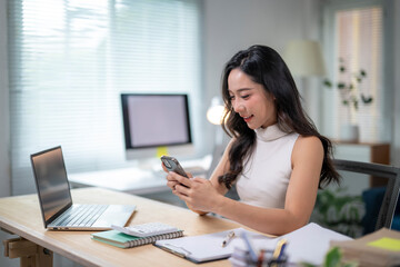 Fototapeta premium Asian businesswoman using smartphone and working with laptop in modern office