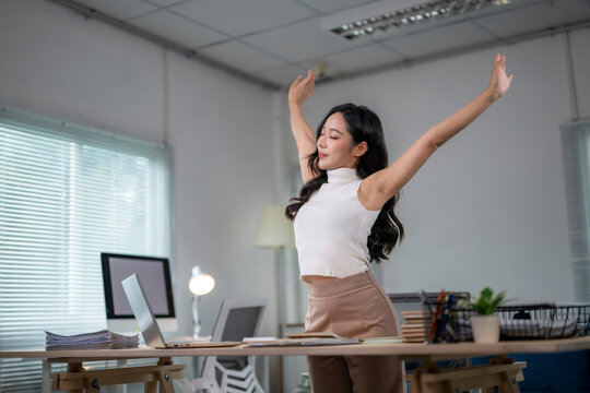Asian businesswoman stretching arms at workplace after work is done