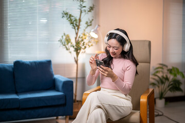 Happy woman listening to music on headphones and using smartphone at home