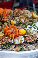 A large seafood platter with a variety of fresh seafood, including oysters, whelks, shrimp, prawns, and scallops, is a presentation of the market's assortment and a tasting set in Paris, France.