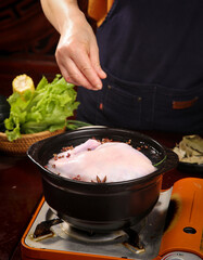 Chef Cooking Whole Raw Chicken with Spices in Traditional Black Pot on Stove