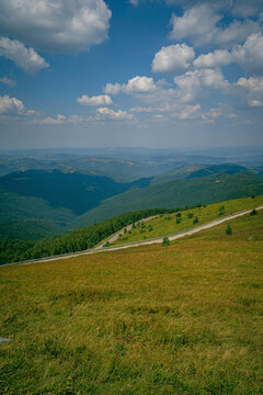Panoramic mountain view in Greece with rolling green hills open meadow and winding road under blue sky with white clouds