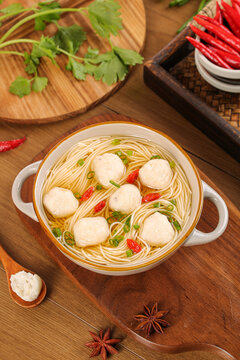 Fishball noodle soup with herbs and spices on wooden table - traditional Asian comfort food