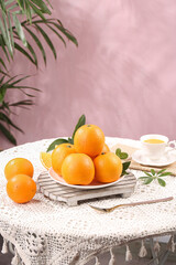Fresh Orange Citrus Fruits on Vintage Table with Tea Cup and Palm Leaves Pink Background