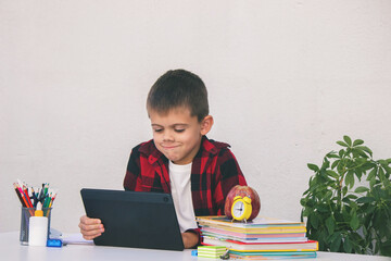 Boy studying remotely. Boy studying with books and his digital tablet at home