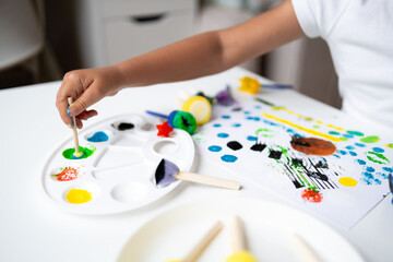 Child painting with colorful paints and tools on white table