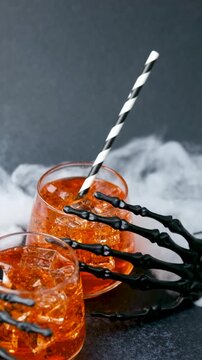 Halloween spooky drinks with ice and skeleton hand decoration and straw in dark setting
