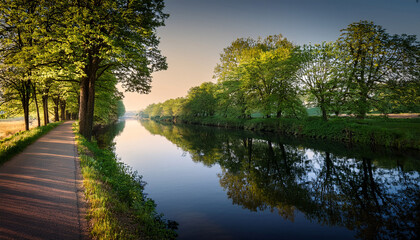 Walking Path Lined With Trees Beside Calm River In The Late Afternoon