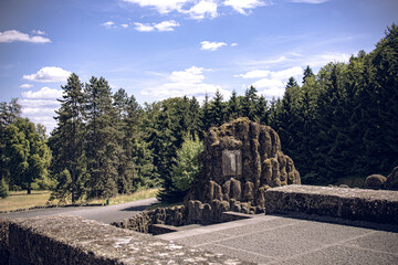Old stone structure covered with moss surrounded by lush green forest under bright summer sky