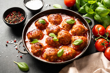Meatballs in tomato sauce in iron plate on black background.