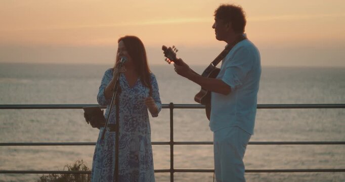 Musical duo performing by ocean during colorful sunset